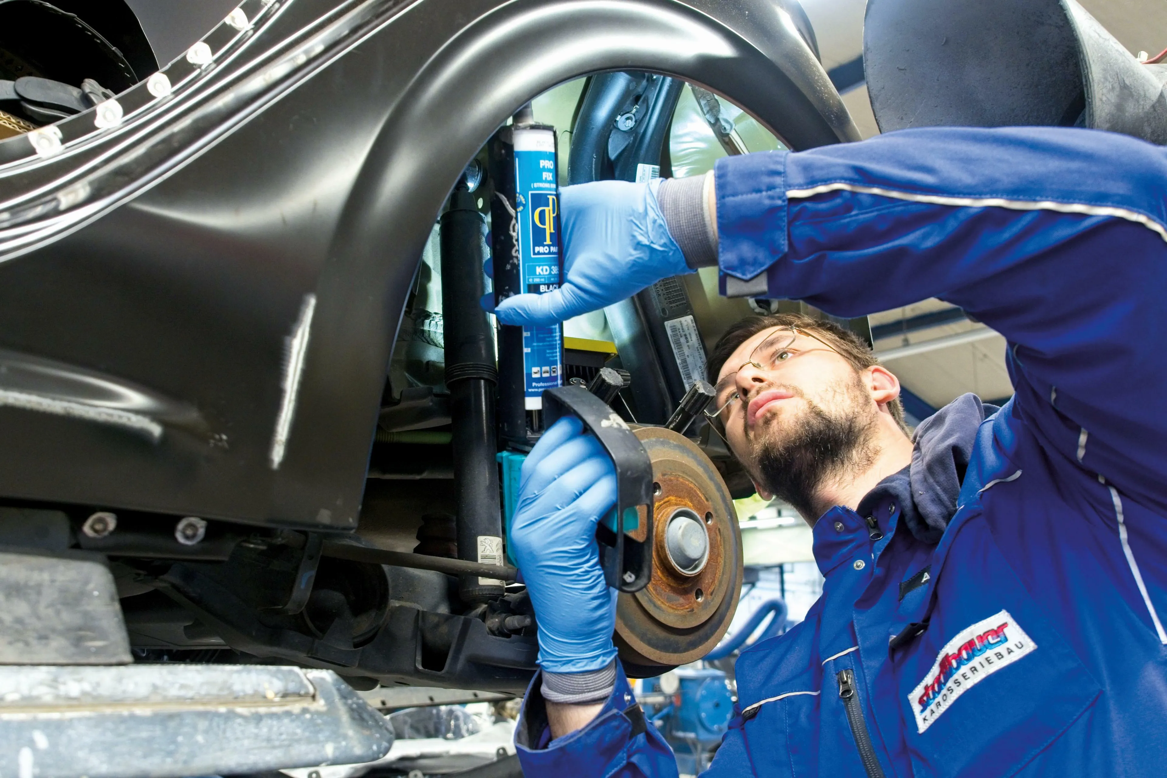 Automechanliker führt als Autoservice das Abdichten von Teilen am Unterboden aus.