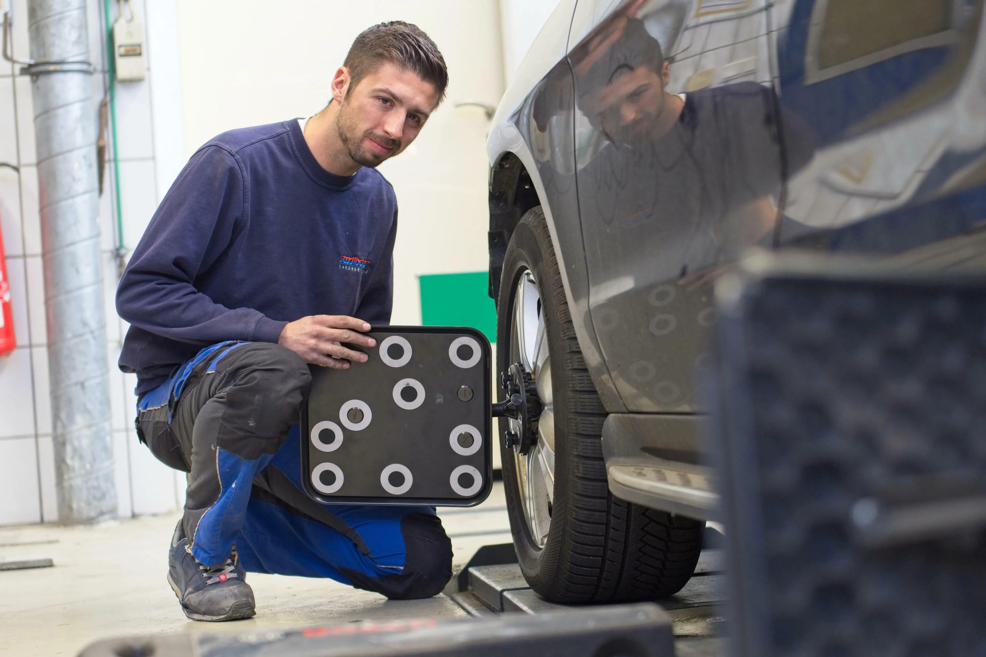 Bild zeigt einen Mitarbeiter, der eine Justierungstafel, die an der Reifenaufhängung des Vorderrades befestigt ist,hält, zur elektronischen Einmessung der Vorderachse