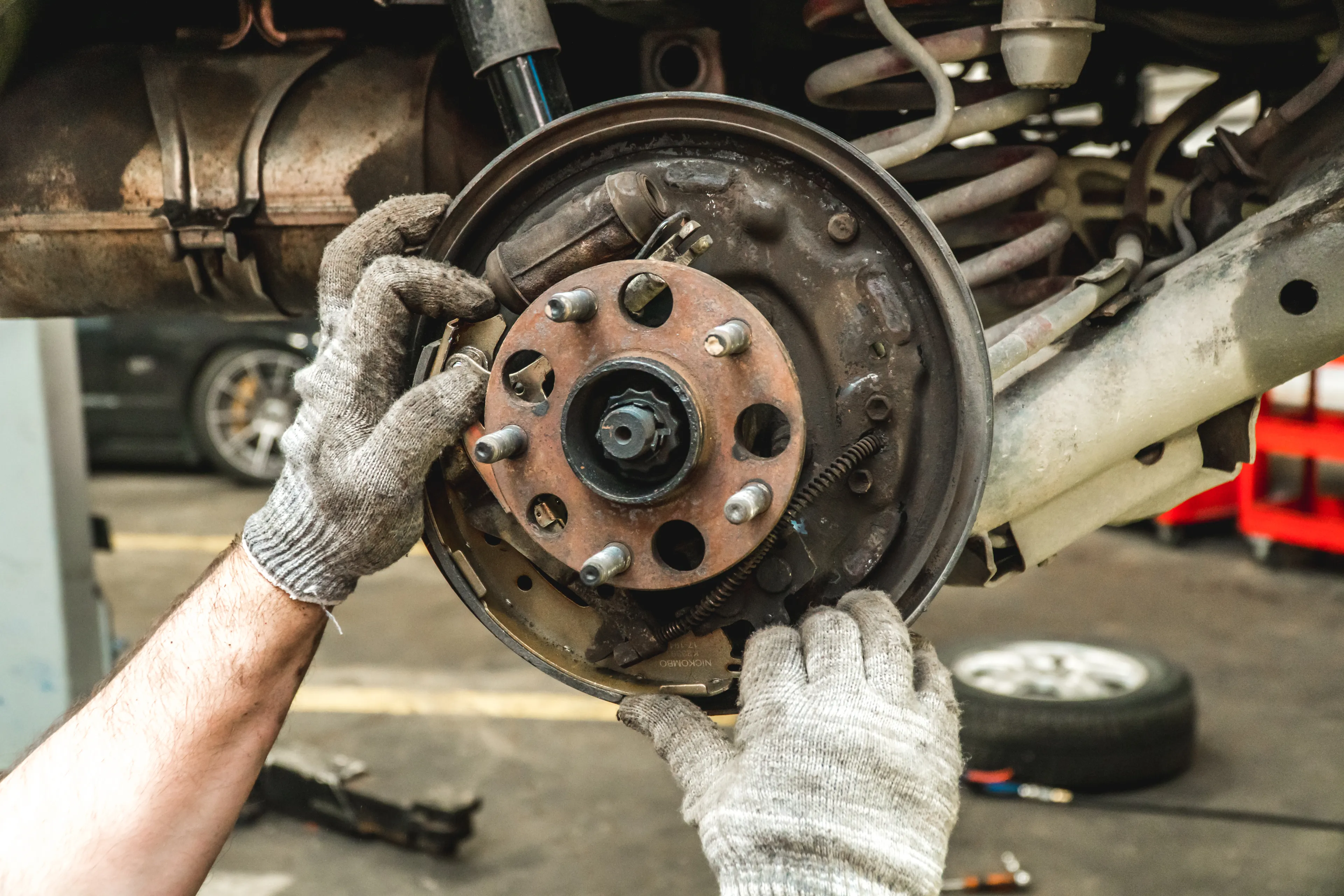 Das Bild zeigt nur die Hände eines KFZ Mechanikers, der Bremsscheibe und Bremsbelege wechselt
