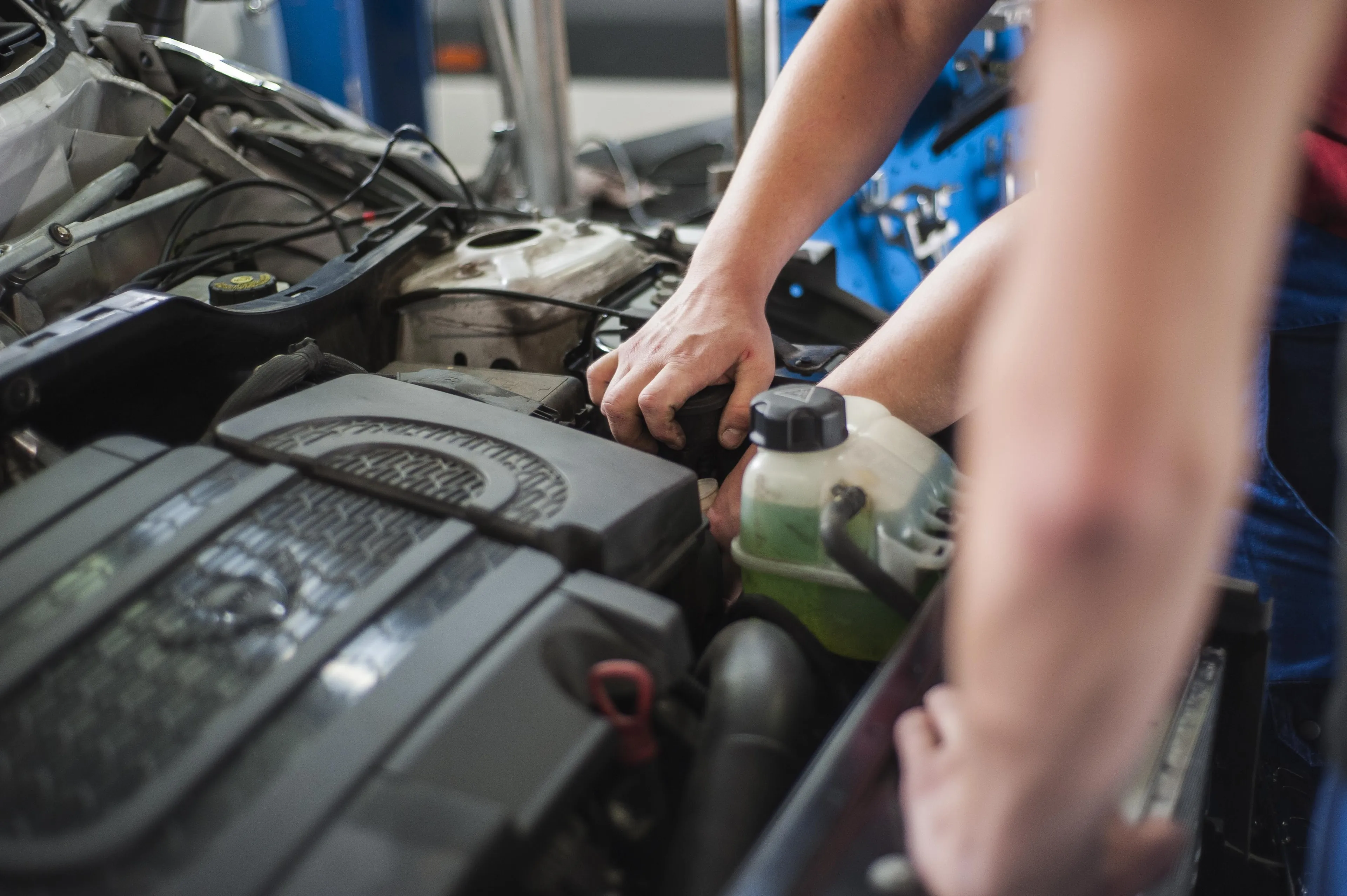 Automechaniker, bei denen nur die Hände und Arme zu sehen sind haben die Motorraumhaube geöffnet und einer dreht eine Abdeckung auf.