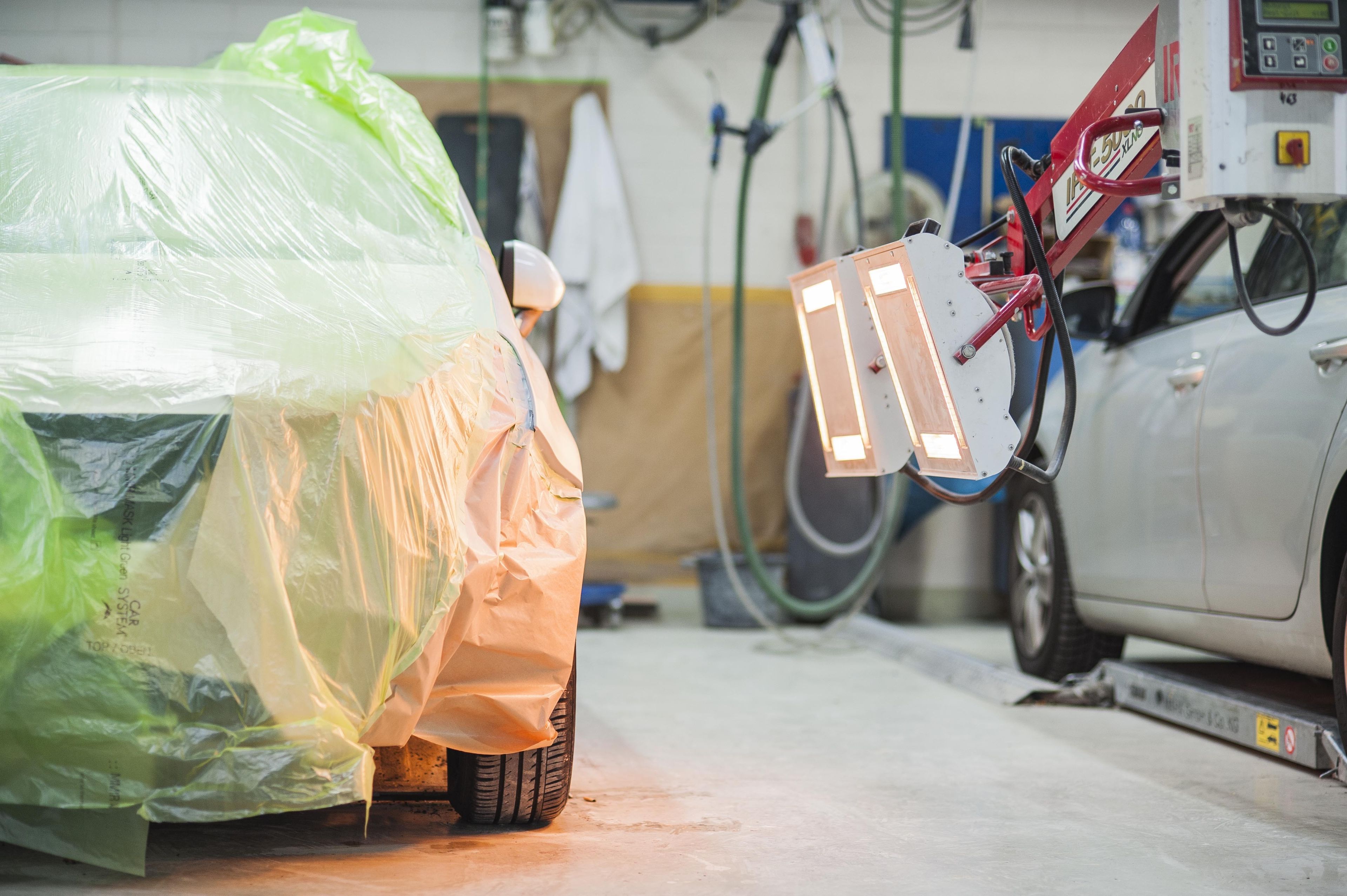 Bild zeigt ein abgeklebtes Auto beim die die neu lackierte Stelle mit Wärmelampen getrocknet wird.