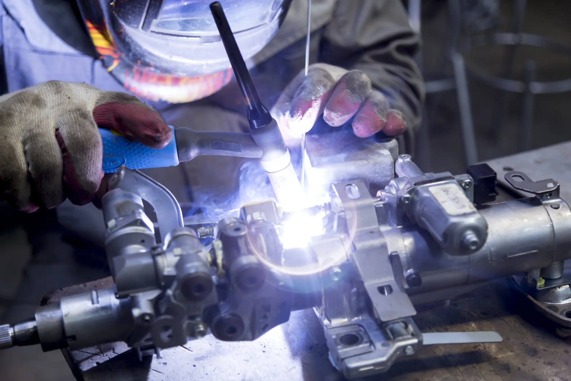 Bild zeigt einen Mechaniker, der an einem Karosserieteil aus Aluminiumschweißt